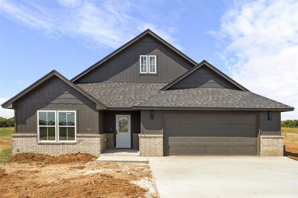 Modern single-family home in Stillwater, OK featuring dark exterior siding, brick accents, two-car garage, and front entryway with glass door under a gabled roof.