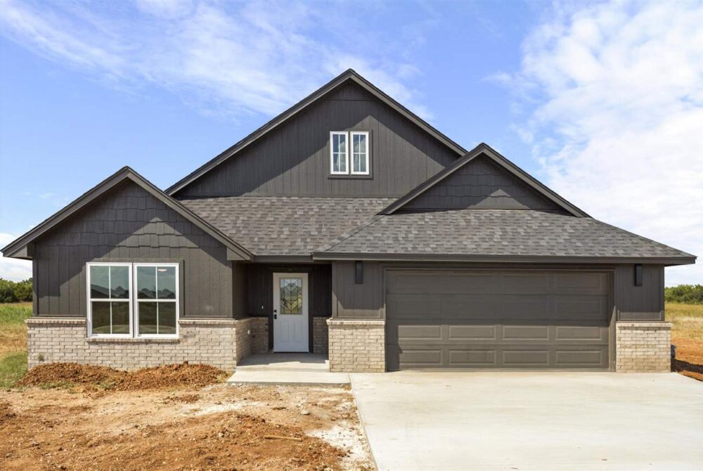 Brand new modern 4-bedroom home for sale in Stillwater, OK featuring dark exterior siding, brick accents, two-car garage, and spacious half-acre lot.