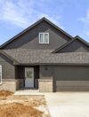 Brand new modern 4-bedroom home for sale in Stillwater, OK featuring dark exterior siding, brick accents, two-car garage, and spacious half-acre lot.