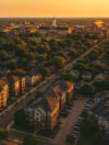 Aerial view of the Stillwater University District at golden hour, showcasing multi-family housing, tree-lined streets, and the Oklahoma State University campus in the background